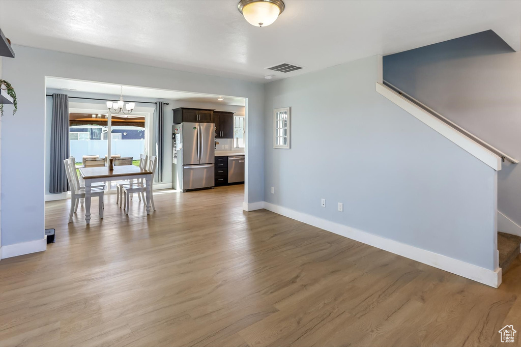 Unfurnished living room featuring visible vents, baseboards, a notable chandelier, light wood-style floors, and stairs