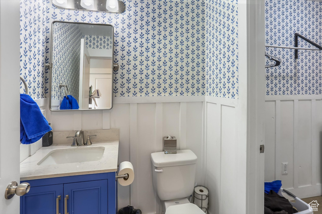 Bathroom with wainscoting, vanity, toilet, a decorative wall, and wallpapered walls