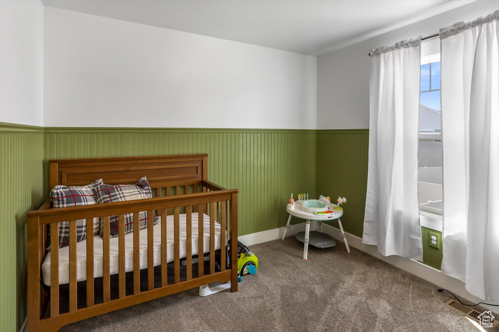 Bedroom featuring visible vents, a wainscoted wall, baseboards, a crib, and carpet floors