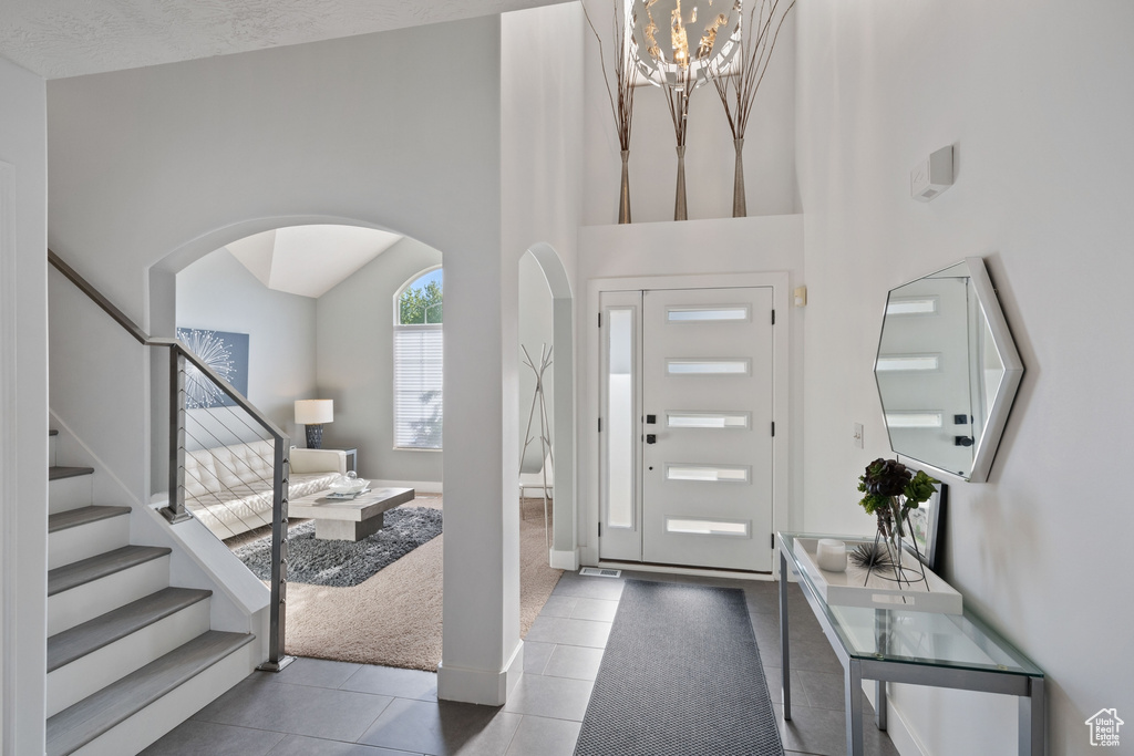 Tiled entrance foyer with an inviting chandelier, arched walkways, stairs, and a towering ceiling