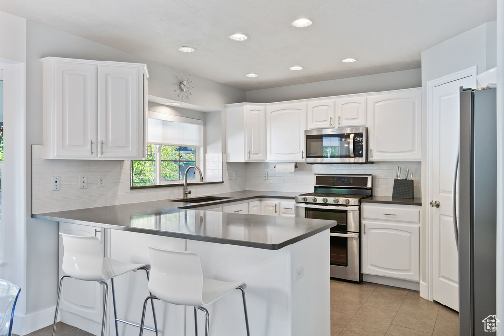 Kitchen with appliances with stainless steel finishes, white cabinetry, a sink, a peninsula, and light tile patterned flooring