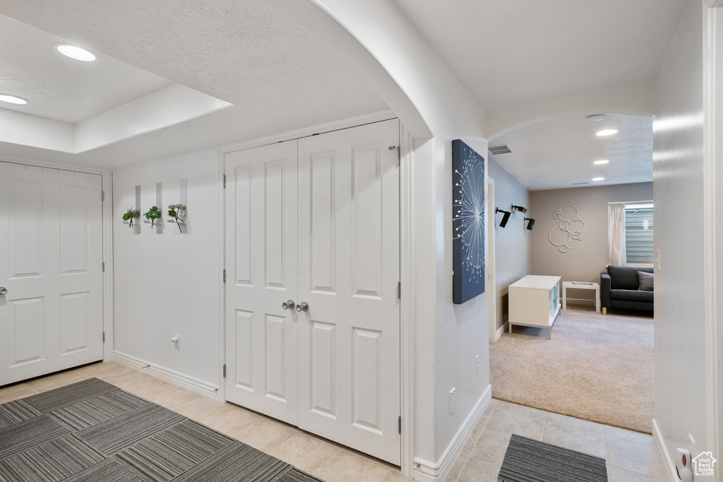 Hallway with light tile patterned flooring, light colored carpet, arched walkways, recessed lighting, and baseboards
