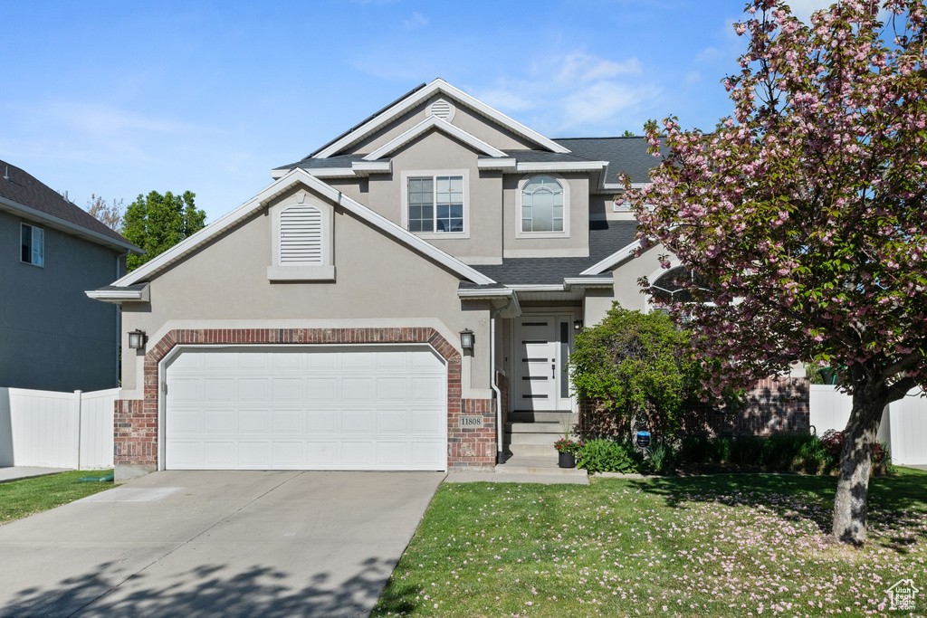 View of front facade featuring fence, brick siding, a garage, a front yard, and driveway