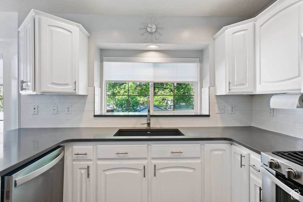 Kitchen with dark countertops, plenty of natural light, white cabinetry, a sink, and stainless steel appliances