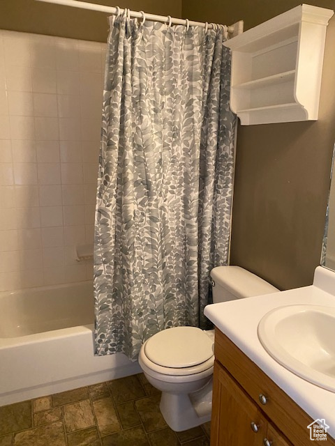 Bathroom featuring vanity, shower / tub combo with curtain, stone finish floor, and toilet