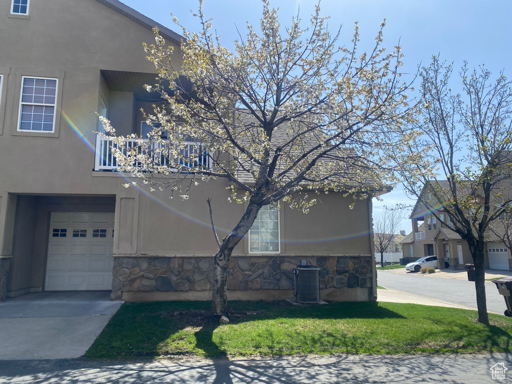 View of side of property featuring a garage, central air condition unit, a balcony, stone siding, and stucco siding
