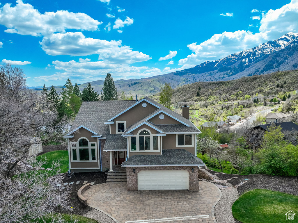 View of front of property featuring roof with shingles, an attached garage, a mountain view, a chimney, and decorative driveway