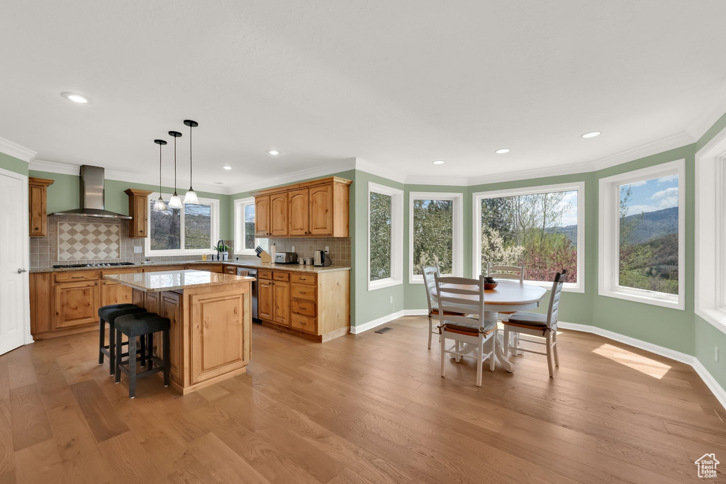 Kitchen with wall chimney range hood, a kitchen bar, a center island, tasteful backsplash, and light wood-style floors