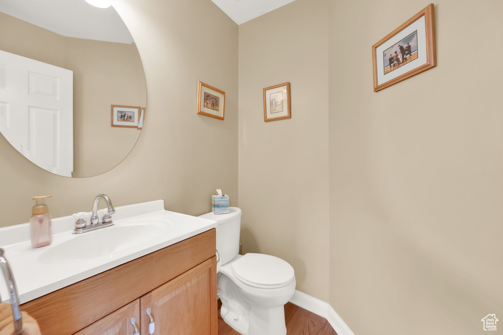 Bathroom featuring vanity, baseboards, wood finished floors, and toilet