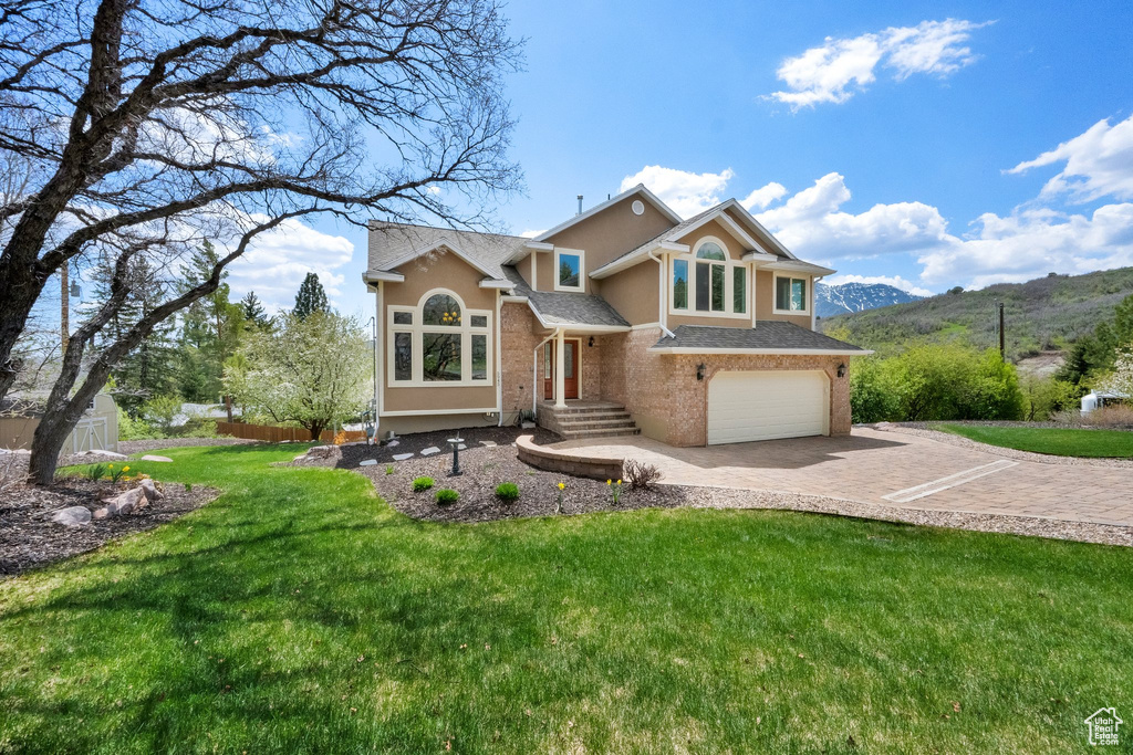View of front facade featuring driveway, a front yard, a garage, a mountain view, and stucco siding