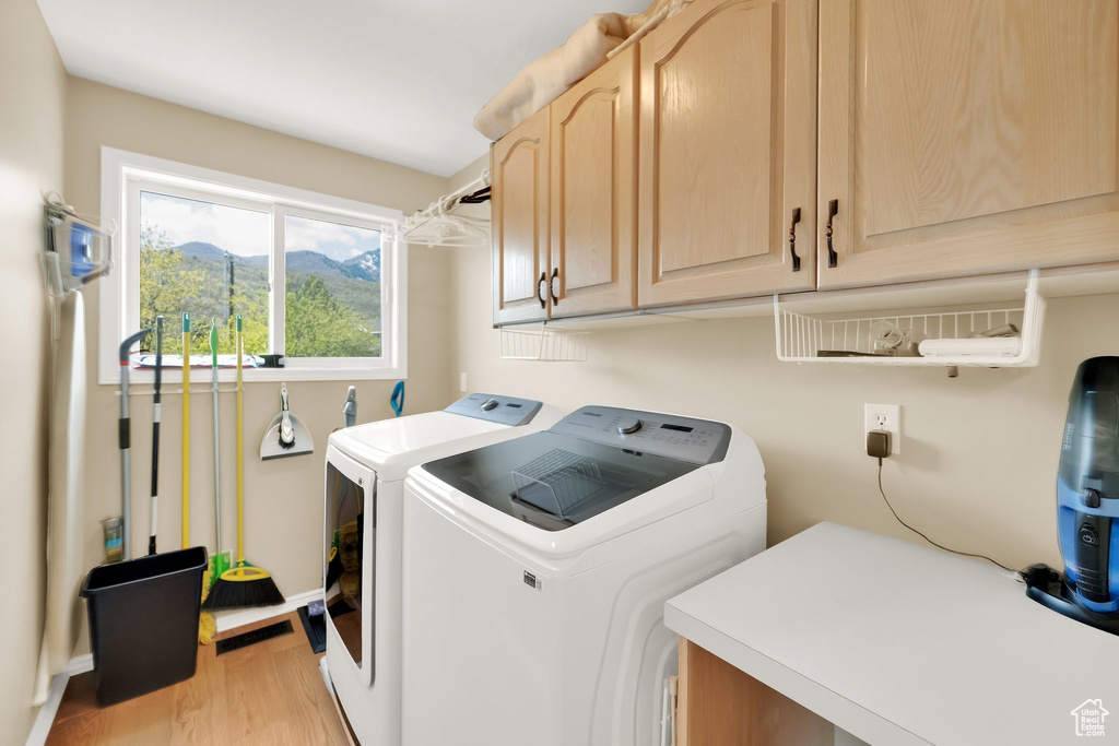 Washroom with cabinet space, washing machine and clothes dryer, baseboards, light wood-type flooring, and a mountain view