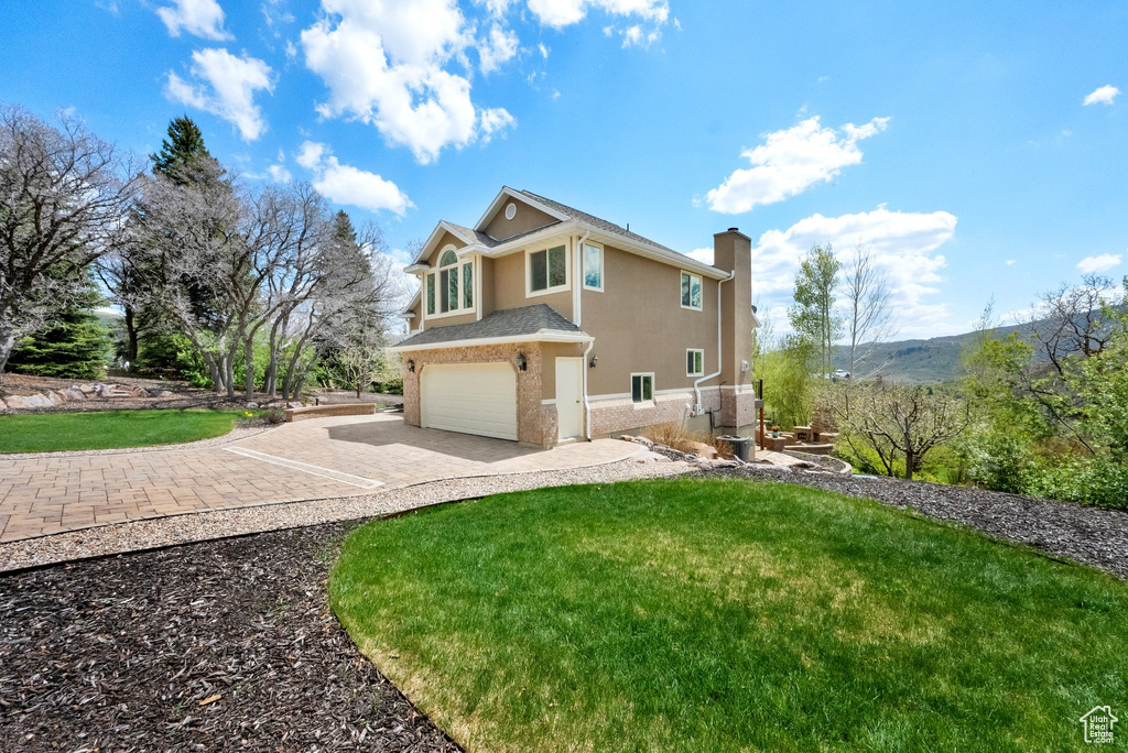 View of side of home featuring an attached garage, stucco siding, a chimney, a lawn, and driveway