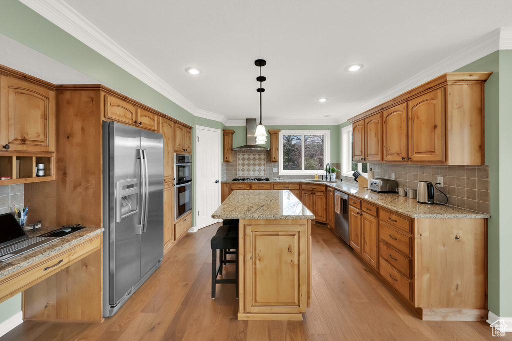 Kitchen featuring decorative backsplash, a center island, ornamental molding, stainless steel appliances, and wall chimney exhaust hood