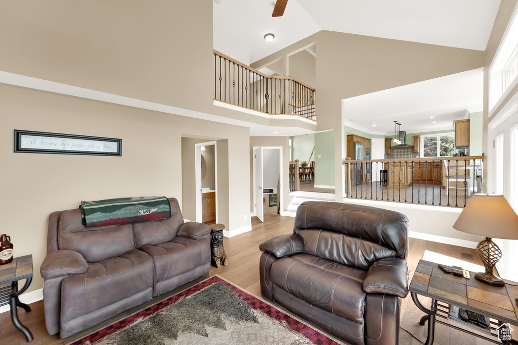 Living room featuring baseboards, ceiling fan, wood finished floors, and a towering ceiling
