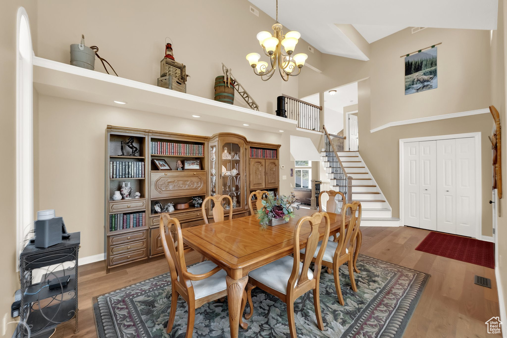 Dining area featuring a high ceiling, a notable chandelier, stairs, baseboards, and wood finished floors