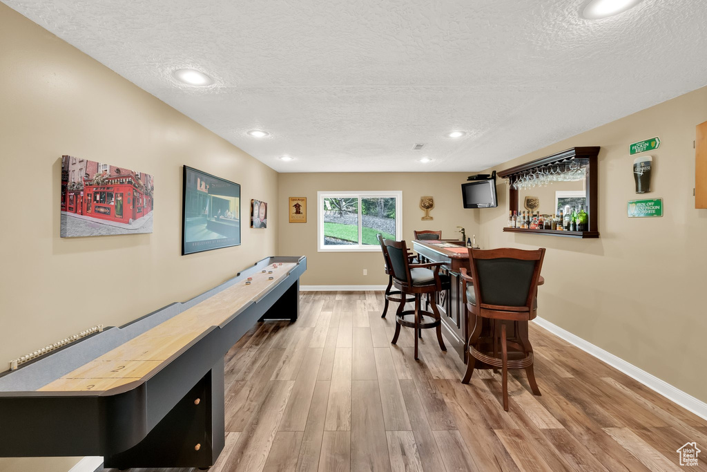 Rec room with bar area, baseboards, a textured ceiling, and wood finished floors