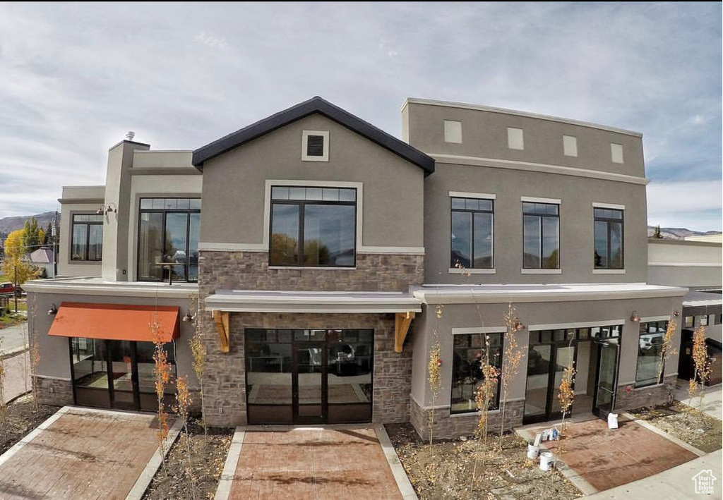 Rear view of property featuring french doors, stone siding, and stucco siding