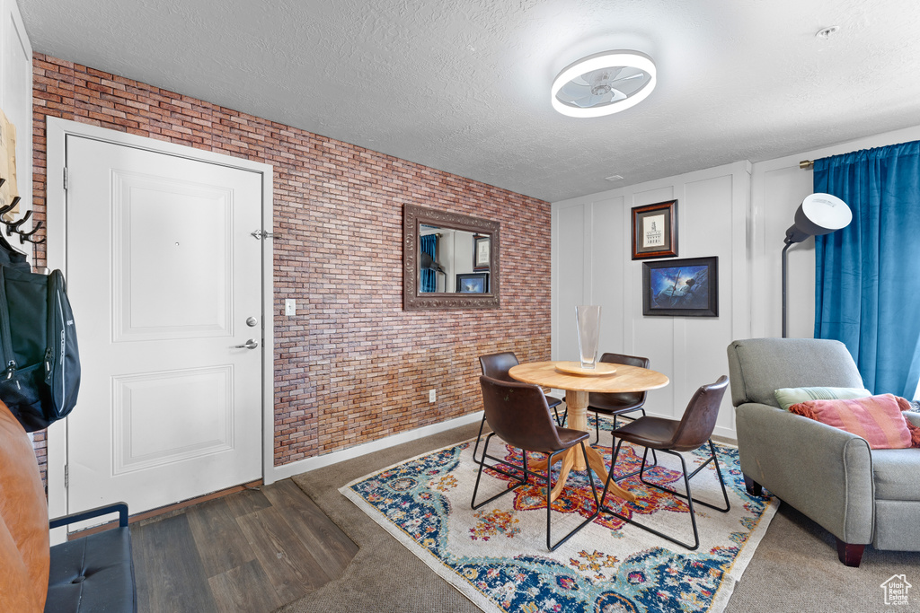 Dining space featuring baseboards, a textured ceiling, wood finished floors, and brick wall