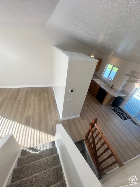 Stairs with a textured ceiling, vaulted ceiling, and wood finished floors