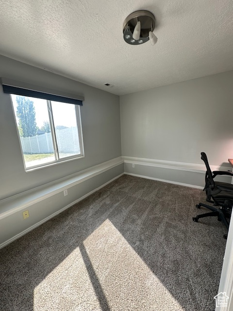 Unfurnished office with a textured ceiling, visible vents, baseboards, and dark carpet