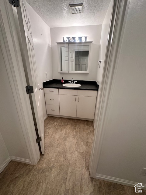 Bathroom featuring visible vents, a textured ceiling, baseboards, and vanity