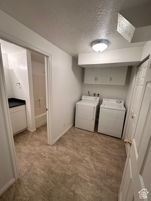Laundry room featuring a textured ceiling, cabinet space, baseboards, light floors, and separate washer and dryer
