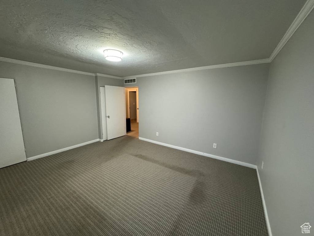 Empty room with a textured ceiling, visible vents, baseboards, ornamental molding, and carpet