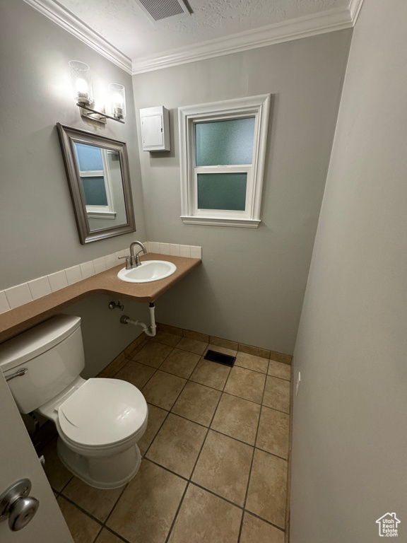 Half bath featuring visible vents, ornamental molding, toilet, tile patterned floors, and a sink