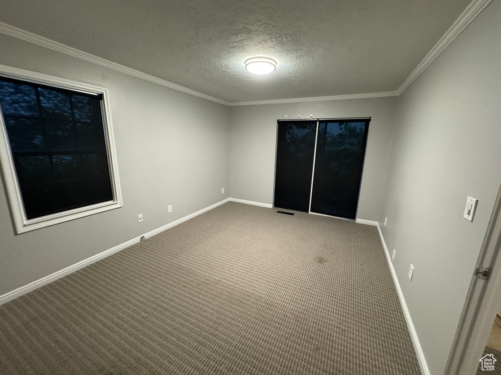Carpeted spare room with crown molding, a textured ceiling, baseboards, and visible vents