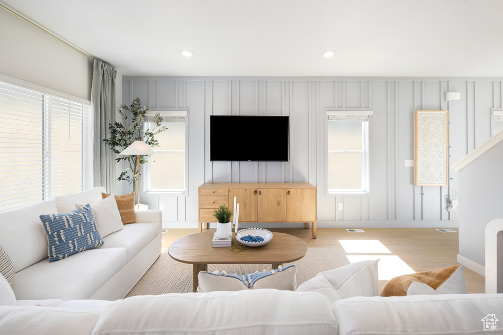 Living area featuring visible vents, light wood-type flooring, baseboards, a decorative wall, and recessed lighting