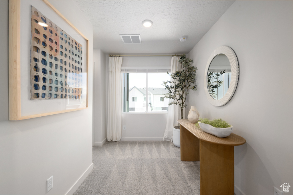 Hallway with baseboards, carpet floors, a textured ceiling, and visible vents