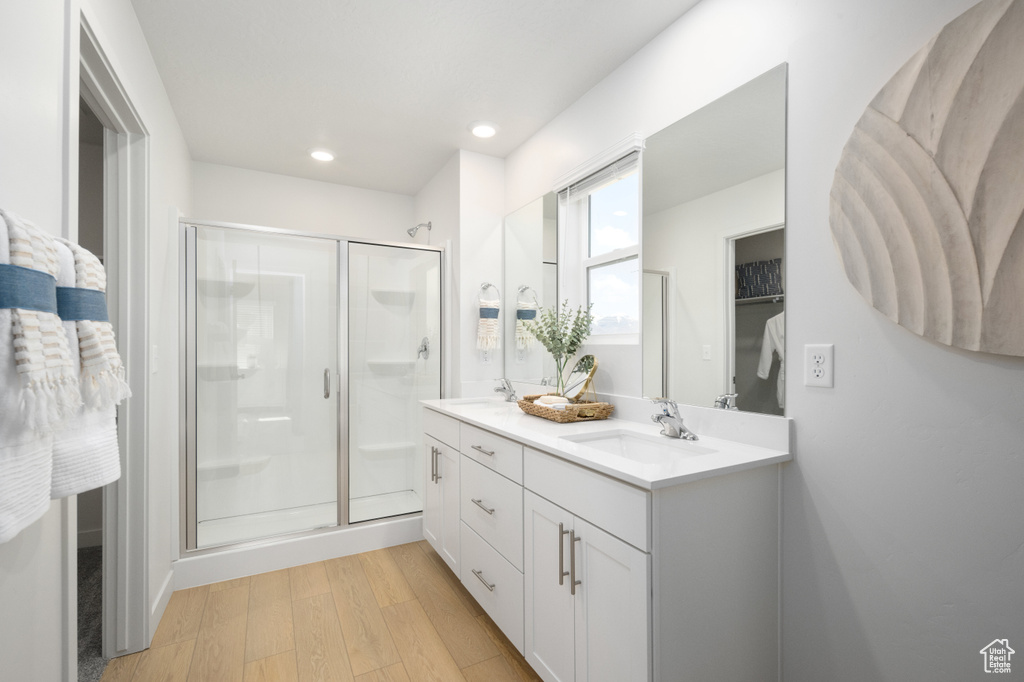 Bathroom with a sink, double vanity, recessed lighting, a shower stall, and wood finished floors