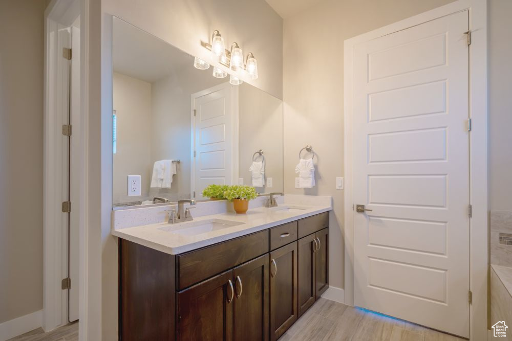 Full bath with double vanity, a sink, and wood finished floors