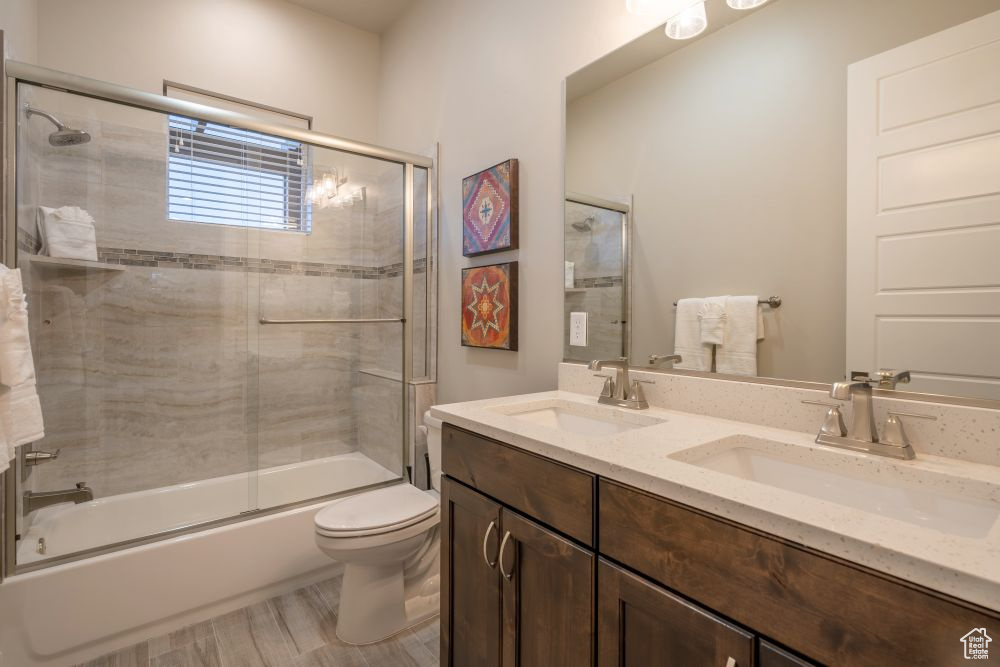 Bathroom with a sink, enclosed tub / shower combo, toilet, and double vanity