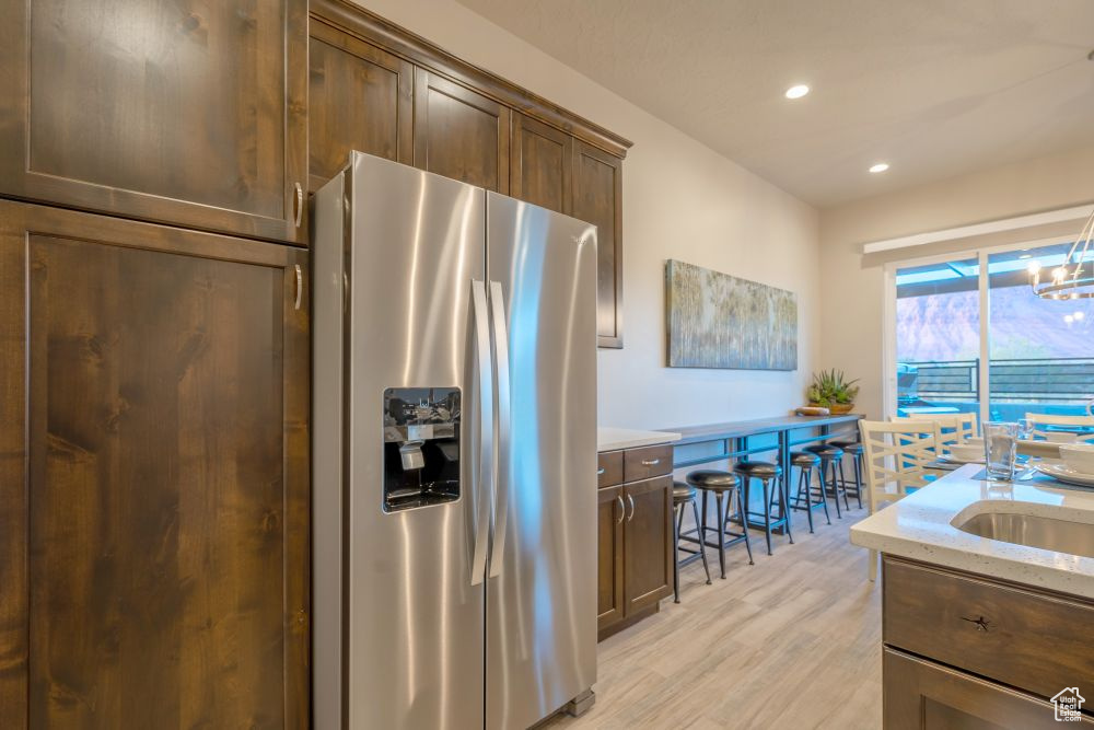 Kitchen featuring light stone countertops, dark brown cabinets, stainless steel fridge with ice dispenser, light wood-style floors, and recessed lighting
