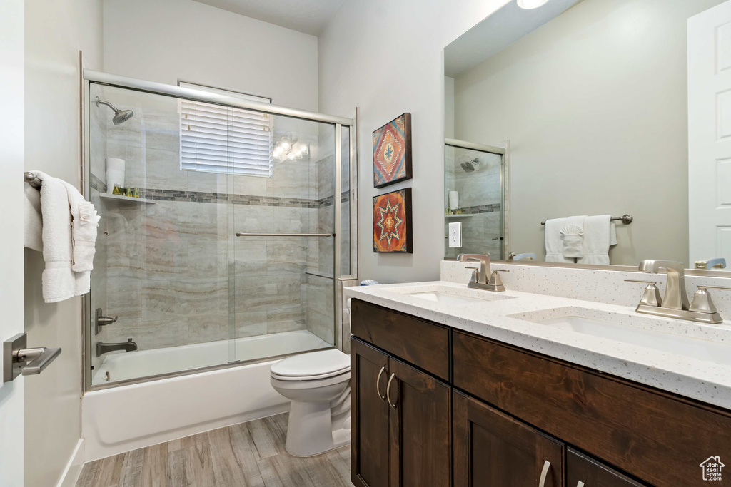Bathroom featuring toilet, enclosed tub / shower combo, wood finished floors, and double vanity