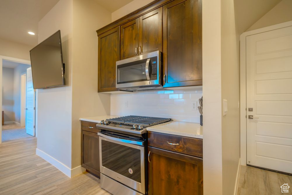 Kitchen with baseboards, appliances with stainless steel finishes, decorative backsplash, and light wood-style flooring