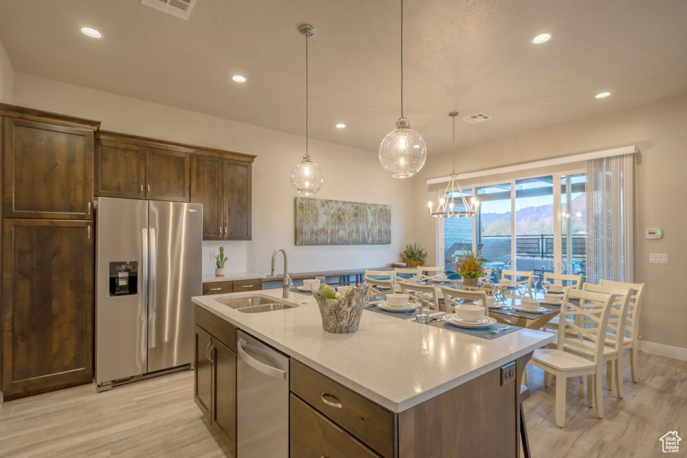 Kitchen with stainless steel appliances, a center island with sink, a sink, and light wood-style floors