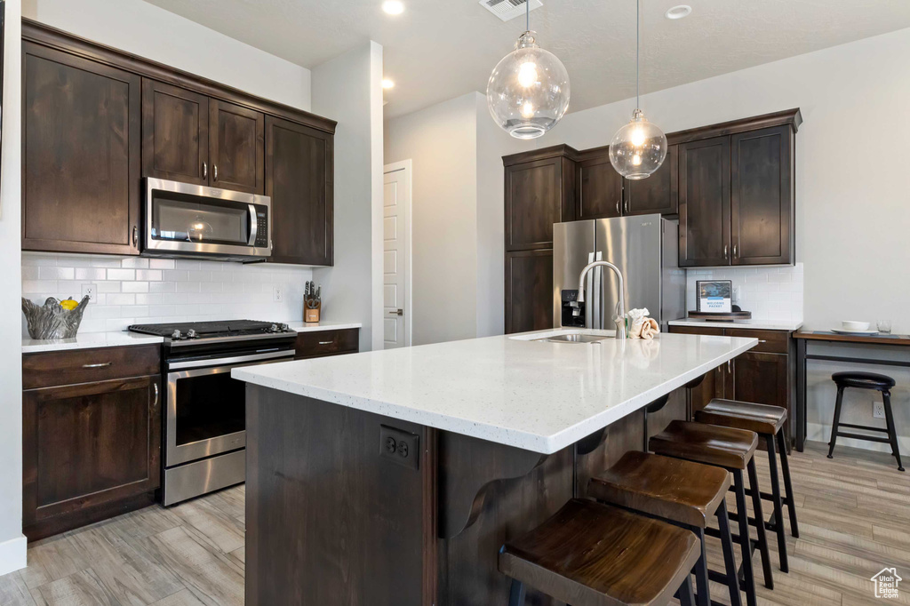 Kitchen featuring stainless steel appliances, a sink, dark brown cabinetry, tasteful backsplash, and a center island with sink