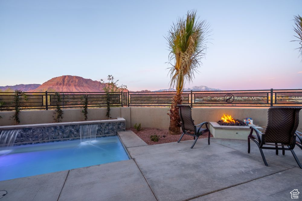 Pool at dusk with a patio, a fenced backyard, a fenced in pool, an outdoor fire pit, and a mountain view