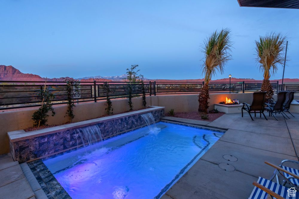 Pool at dusk featuring a fenced in pool, a fenced backyard, a fire pit, and a patio area
