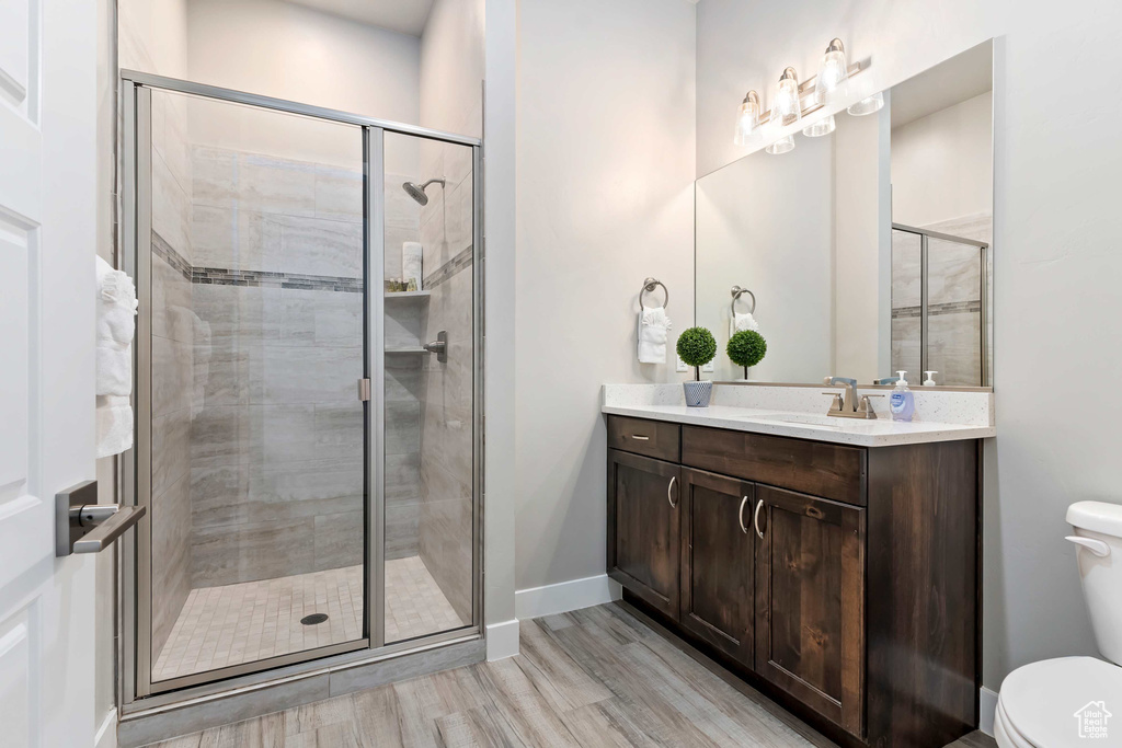 Full bathroom with toilet, wood finished floors, a stall shower, vanity, and baseboards