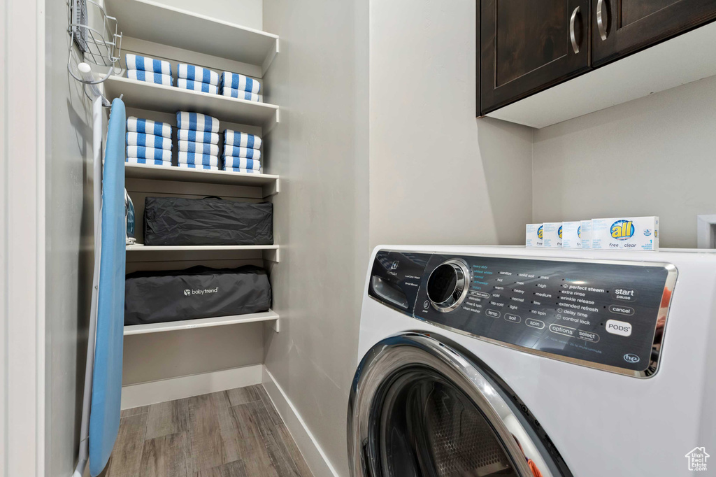 Clothes washing area with wood finished floors, cabinet space, baseboards, and washing machine and dryer