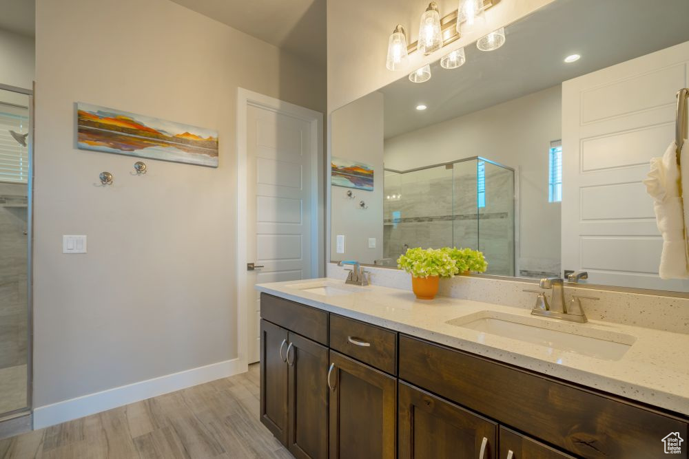 Full bathroom featuring double vanity, a shower stall, a sink, and wood finished floors