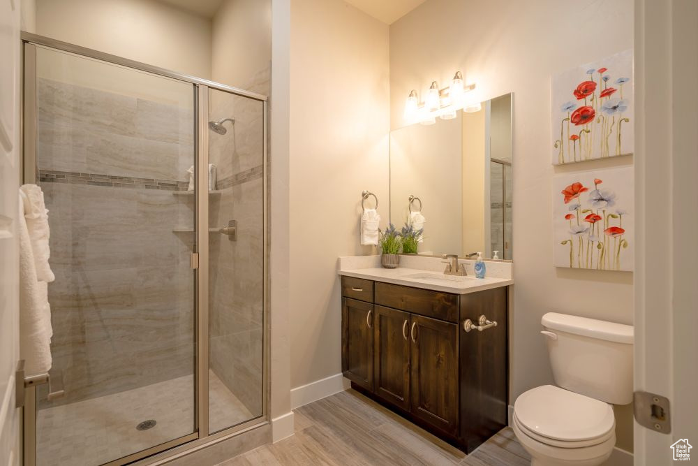 Full bathroom with vanity, toilet, baseboards, a shower stall, and wood finished floors