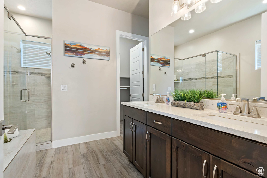 Bathroom with a shower stall, wood finished floors, double vanity, baseboards, and recessed lighting