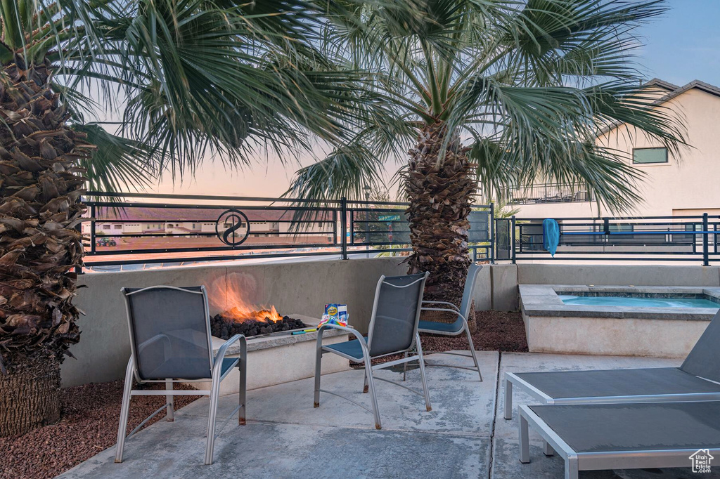 Patio terrace at dusk featuring an in-ground hot tub, a fire pit, and fence