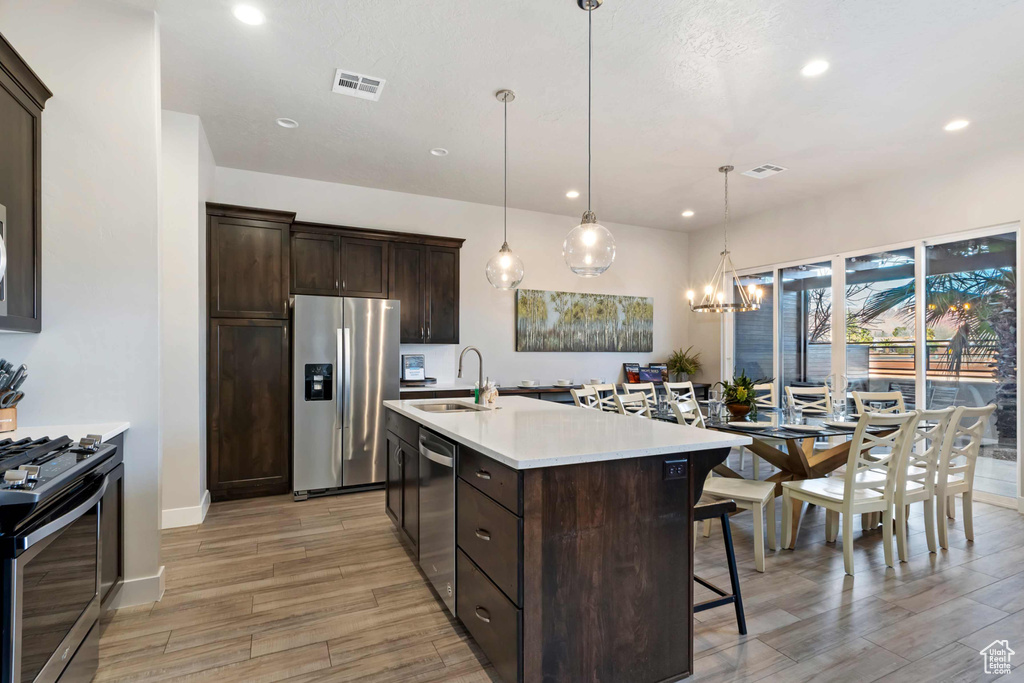 Kitchen with stainless steel appliances, a sink, light wood-type flooring, dark brown cabinetry, and a kitchen breakfast bar