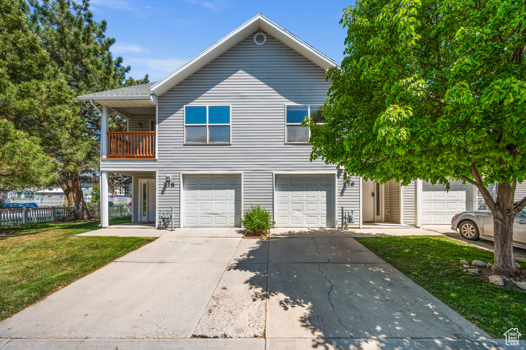 View of front of home with a front yard, a garage, fence, a balcony, and concrete driveway
