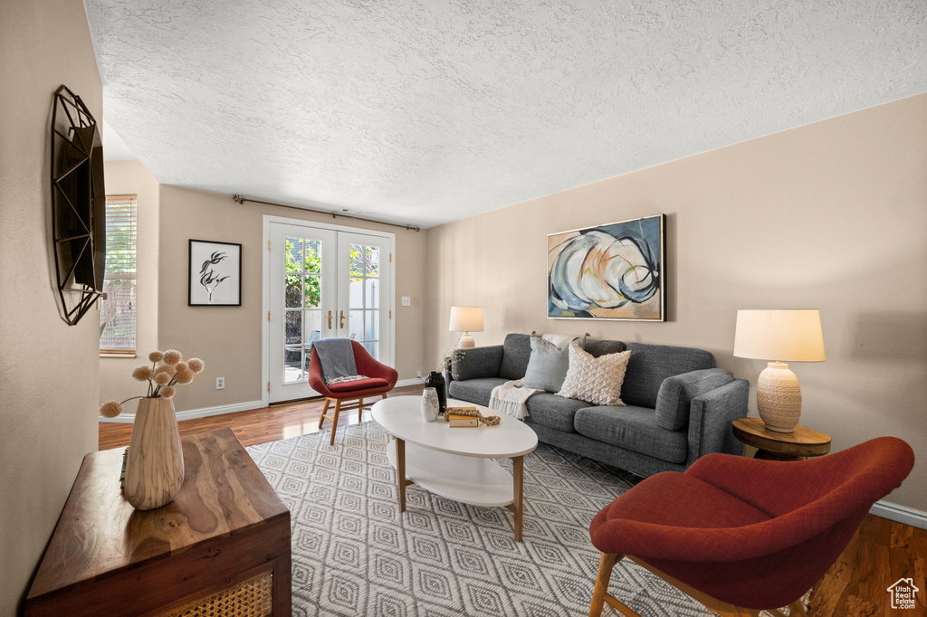 Living room featuring light wood-style floors, baseboards, french doors, and a textured ceiling